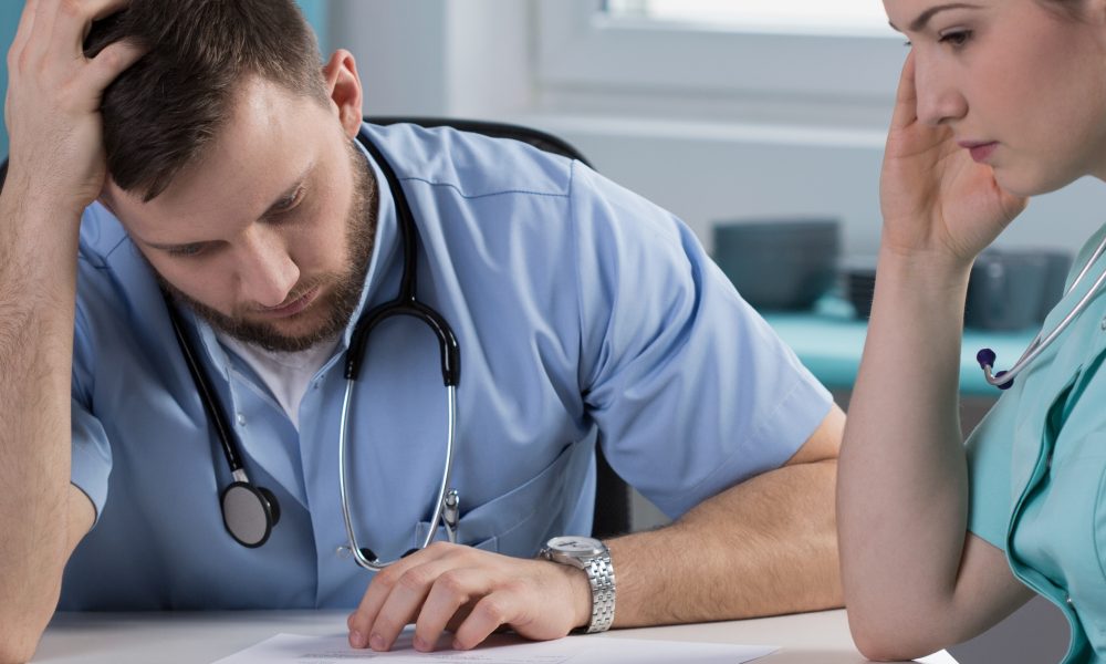 Two medical professionals review paperwork with worried expressions.