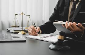 Lawyer writing notes at a desk with legal books, scales, and a gavel.